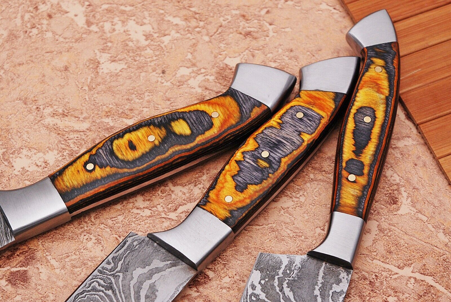 Handmade Damascus chef knife set with pakka wood handles displayed on a tiled and wood surface