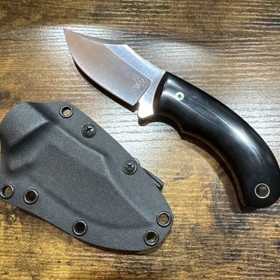 Heritage Forge 3.5" Clip Point Skinner with black wood handle and leather sheath on wooden surface.